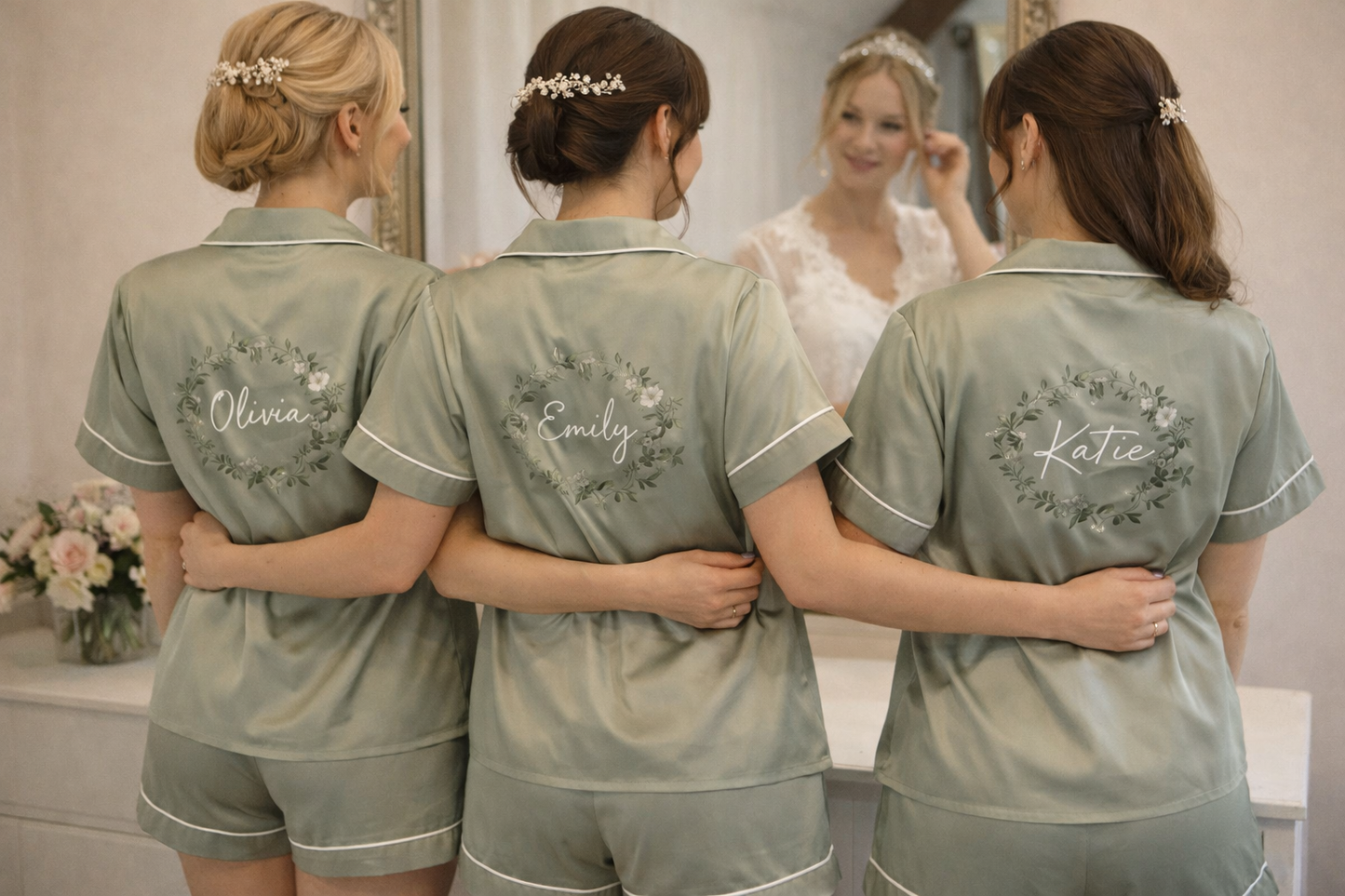 Three women in matching green pajamas with names and roles on the back, standing in front of a mirror.